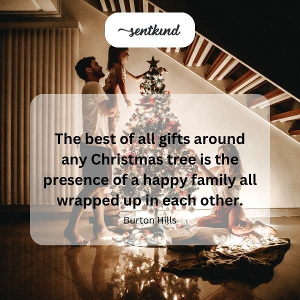 A smiling family embraces warmly near a decorated Christmas tree.