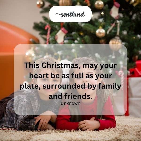 A warmly lit Christmas dinner table is laden with food, surrounded by smiling people.