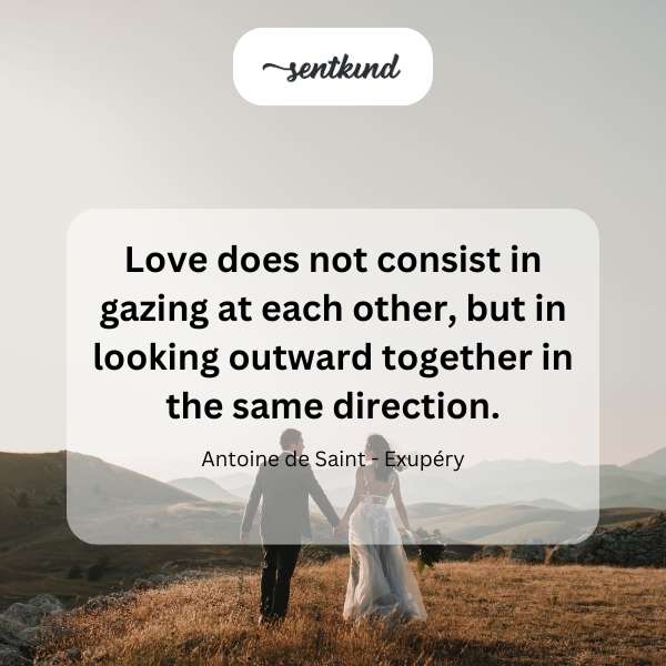 A couple stands on a hilltop, holding hands and looking towards a distant, bright horizon.