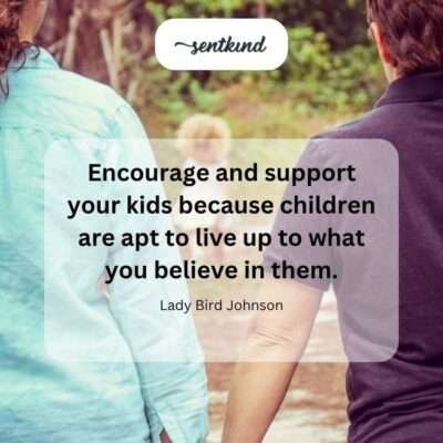 A parent kneels down to gently hold their child's shoulders while offering a warm, encouraging smile and supportive gaze.