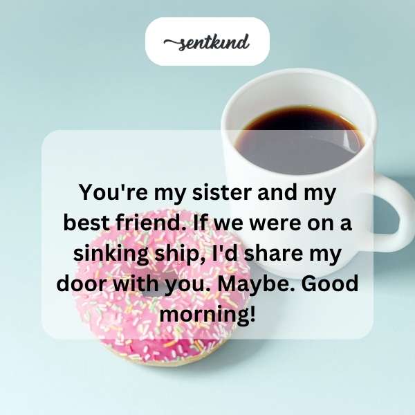 Two young women, one holding a coffee mug, smiling and laughing together on a sofa in a sunlit room.