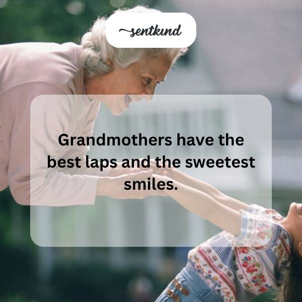 A smiling grandmother sits in a chair with a child comfortably resting on her lap.