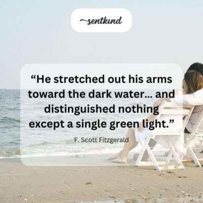 A silhouetted figure stands on shore with arms outstretched towards dark water where a single green light glows in the distance.