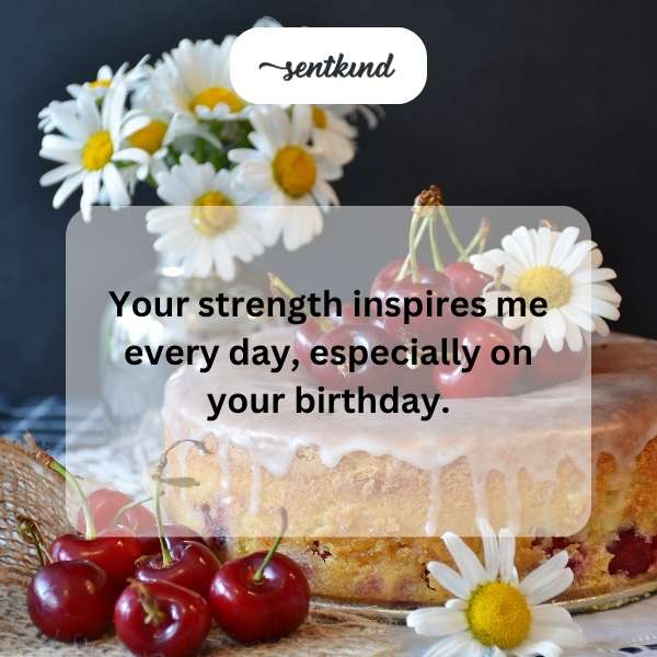 A woman is smiling warmly while holding a birthday cake with lit candles.